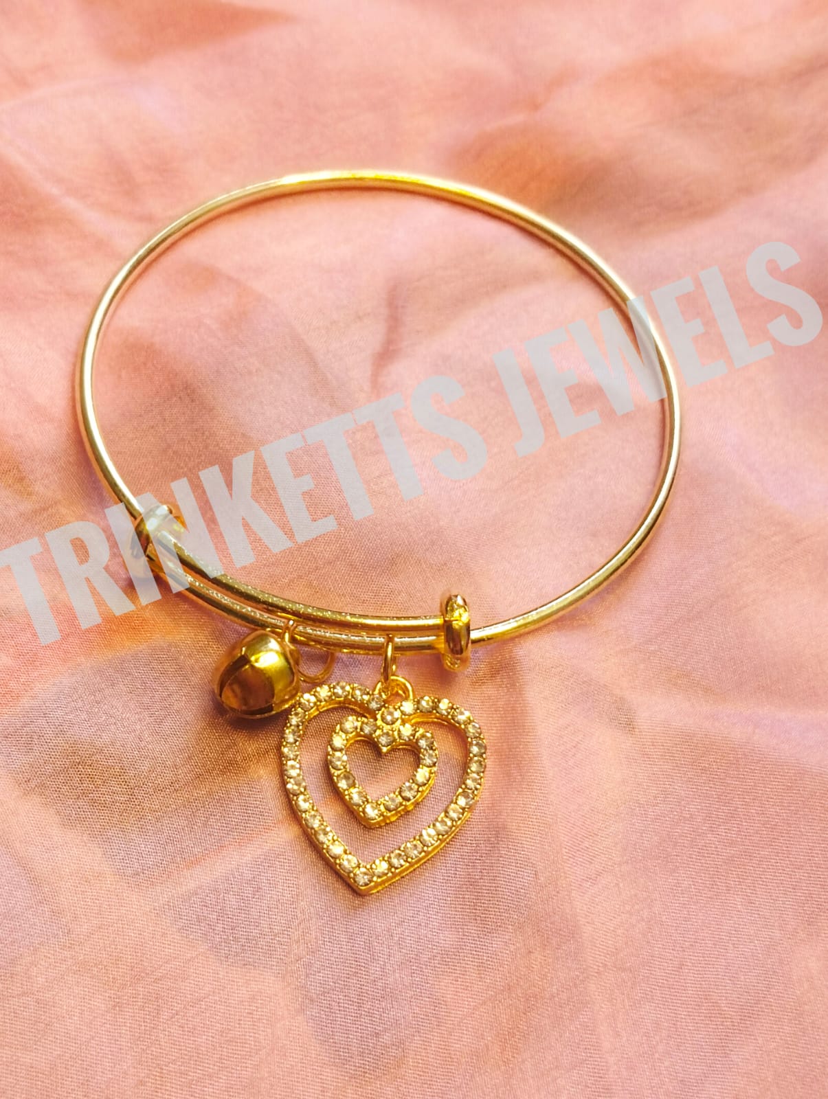Trinketts Golden Charm Bracelet - Heart-shaped design with zircon outlines on a pink background.