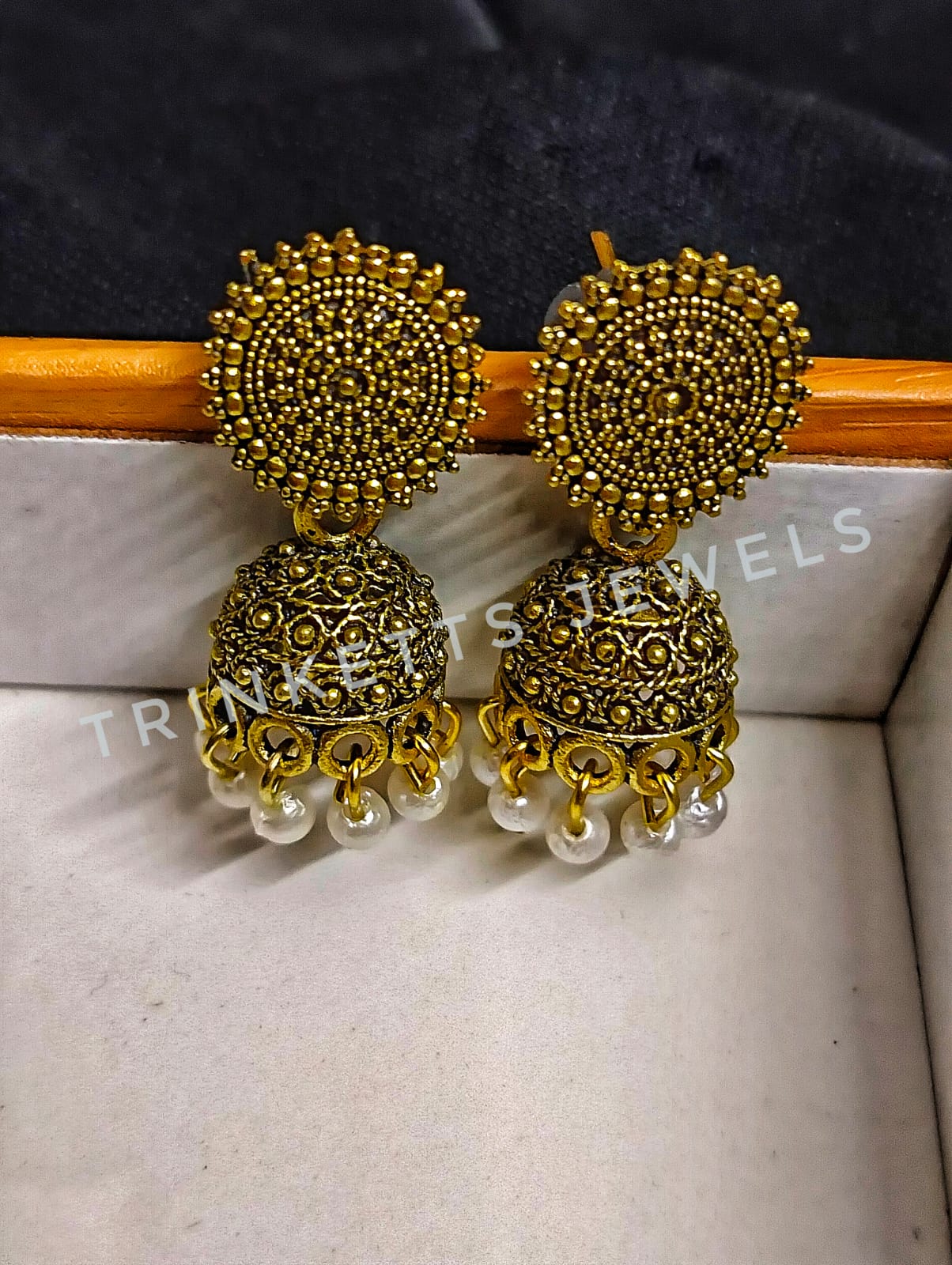 Oxidized golden metal Jhumki earrings, approximately 1.5 inches in size. The design features an intricate circular pattern with a hanging Jhumki plate adorned with white beads. Elegant and timeless, these Jhumkis add a touch of Indian charm to your style